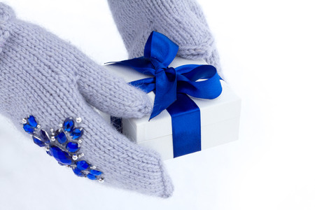 Hands in mittens hold a gift in a box with a blue ribbon.の写真素材