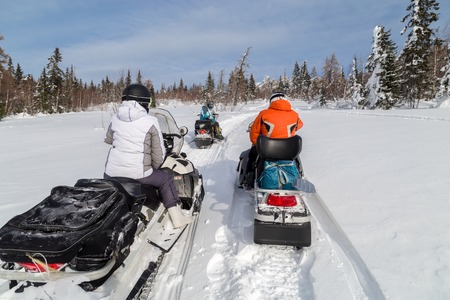 Two men and a woman stopped at a clearing while traveling in the winter woods on snowmobiles.の写真素材