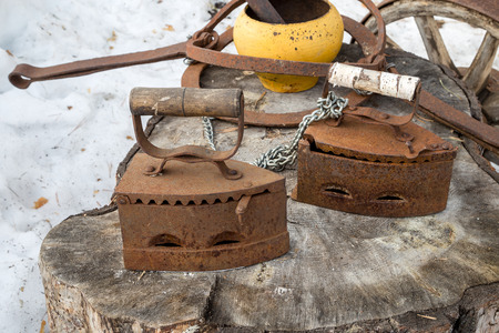 Two old rusty irons on a large wooden stump.の写真素材