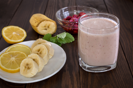Yogurt with banana slices and strawberries and a plate with sliced fruit on a wooden table.の写真素材