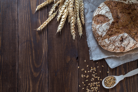 Whole-wheat bread and wheat ears on a wooden table.の写真素材