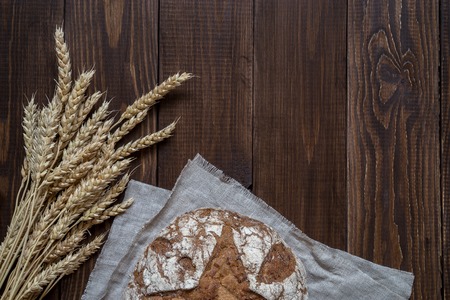 Whole-wheat bread and wheat ears on a wooden table.