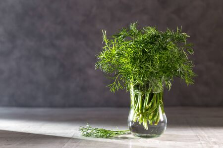 Dill in a transparent vase on a wooden table.