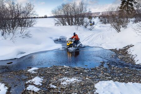 Athletes on a snowmobile forwarded across a river in the mountains of the Urals.の写真素材