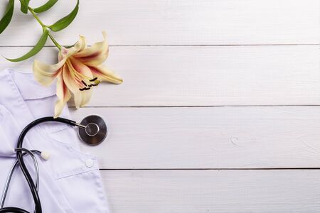 Stethoscope, medical coat and lily on a wooden background.の写真素材
