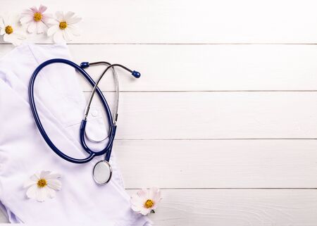 Stethoscope, medical gown and chamomiles on a wooden background.の写真素材