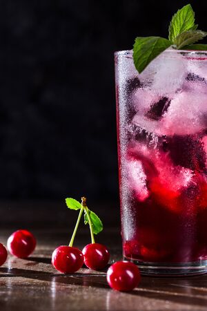 Cherry lemonade with ice in a transparent glass on a dark background.の写真素材