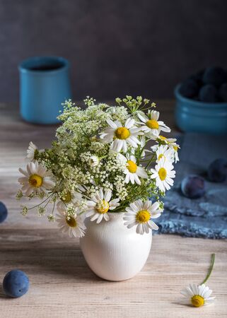 Bouquet of daisies in a vase and plums on a wooden table.の写真素材