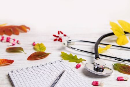Stethoscope, pills and autumn leaves on a wooden background.の写真素材