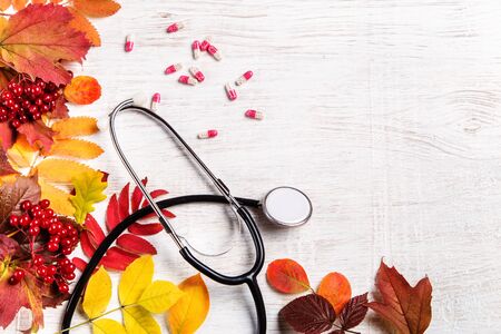Stethoscope, pills and autumn leaves on a wooden background.の写真素材