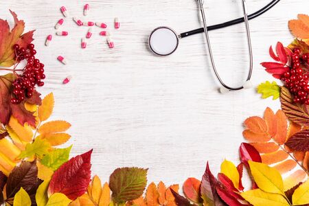 Stethoscope, pills and autumn leaves on a wooden background.の写真素材