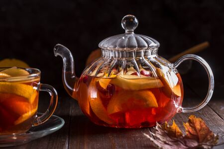 Fruit hot tea with oranges, apples, cranberries and cinnamon in a glass teapot on a wooden table. Healthy hot drink.の写真素材