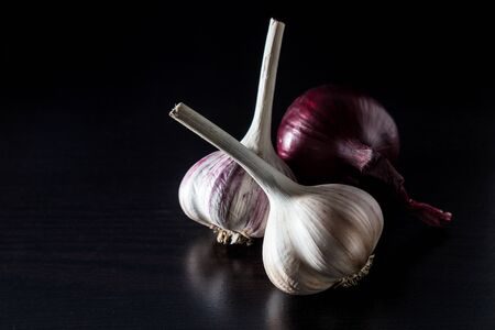 Two garlic heads and onions on a dark background.