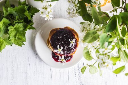A stack of fritters with black currants on a plate on a light background.