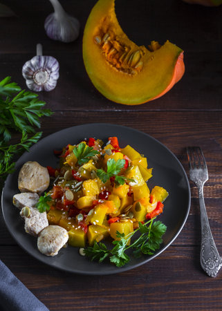 Chicken breast and pumpkin stew with bell peppers, tomatoes, sesame seeds and pumpkin seeds, garnished with parsley.の写真素材