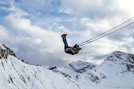 Young sporty girl swinging on a swing over an abyss on snow-capped mountain peaks.の写真素材