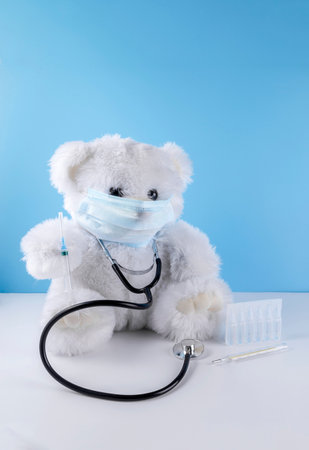 White teddy bear in a mask with a syringe. Childhood vaccination concept with copy space.の写真素材