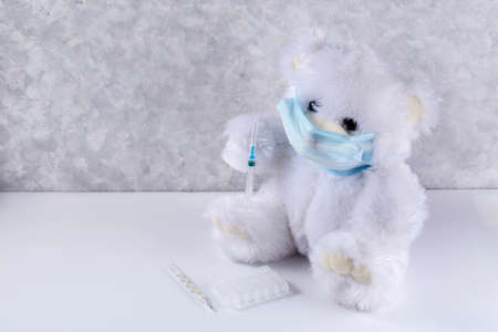 White teddy bear in a mask with a syringe. Childhood vaccination concept with copy space.の写真素材