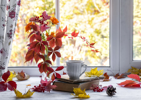 A cup of tea on a wooden windowsill with a bouquet of autumn leaves on a natural background.の写真素材