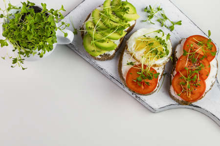 Whole wheat toast with curd cheese, tomatoes, avocado and microgreens. Copy space.