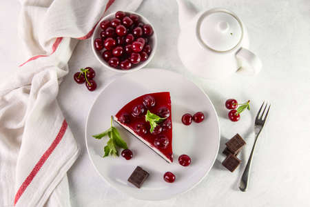 A piece of cherry cheesecake on a plate on a white table.の写真素材
