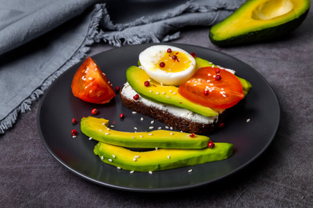 Toast with curd cheese, avocado, boiled egg and tomato on a plate.