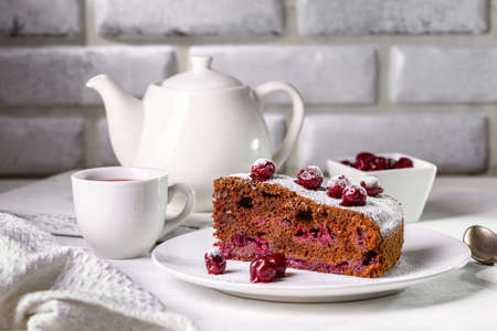 Chocolate tart with cherry and fruit tea in a cup on a light table.