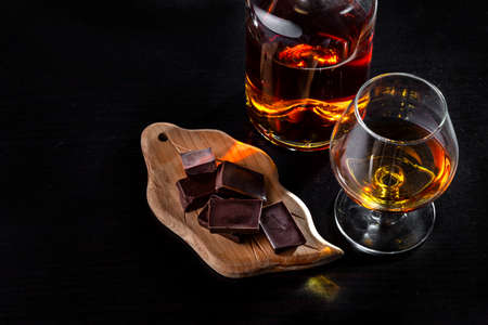 A glass of cognac, cognac in a bottle and pieces of chocolate on a dark background. copyspace.の写真素材