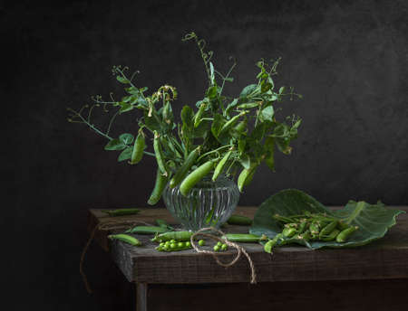 Young fresh green peas in a glass vase on a wooden table. still life.の写真素材