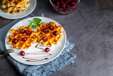 Belgian or Brussels waffles with frozen cherries. Homemade cottage cheese banana waffle in a plate on a dark table. copyspace.の写真素材