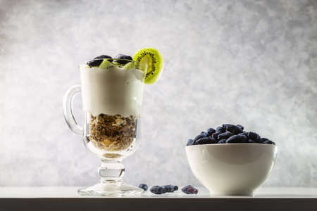 Muesli, yogurt, honeysuckle and kiwi in a transparent glass. Delicious and healthy breakfast.の写真素材