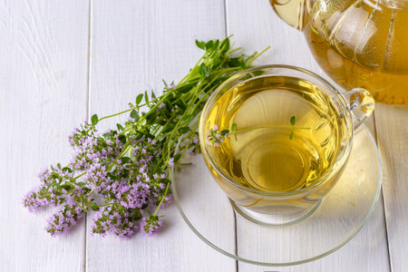 Herbal tea with thyme in a transparent cup and a bouquet of thyme on a white wooden table.の写真素材