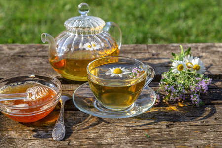 Herbal tea with chamomile and thyme in a transparent cup on an old wooden table on a sunny day.の写真素材