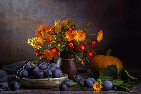 Still life with plums and a bouquet of orange flowers.の写真素材