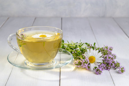 Herbal tea with chamomile and thyme in a transparent cup on a white wooden table.の写真素材