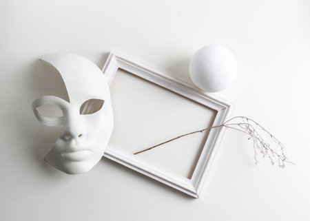 Black and white mass still life: a mask on a white background, a picture frame, abstraction.