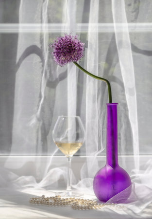 Still life with a flowering decorative bow, wine in a glass and a pearl necklace on a white window sill.の写真素材