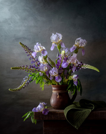 Rustic still life with lupins and irises in a crock on a dark background.の写真素材