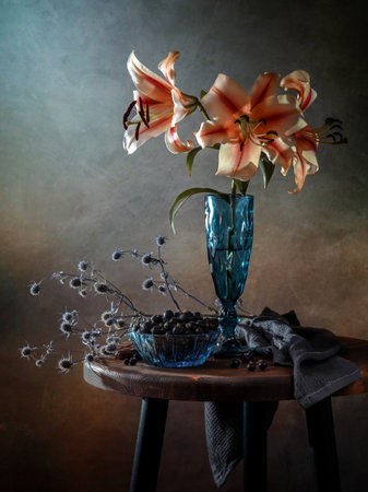 Still life with lilies in a glass vase and black currants on a wooden table.の写真素材