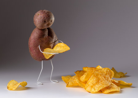 Old potato thoughtfully holding chips. Concept photo.の写真素材