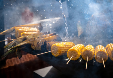 Selective focus of cooking corn and pineapples on a picnic grill on an outdoor barbecue grill with fiery flames and smoke in the open kitchen of an outdoor food restaurant.の写真素材