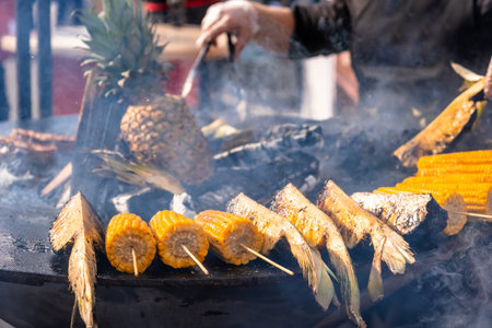 Selective focus of cooking corn and pineapples on a picnic grill on an outdoor barbecue grill with fiery flames and smoke in the open kitchen of an outdoor food restaurant.の写真素材