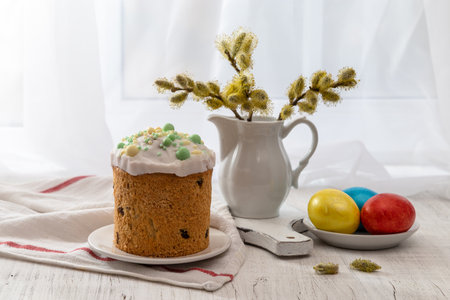 Easter still life with colored eggs, Easter cake and willow in a milk jug on the windowsill on a...