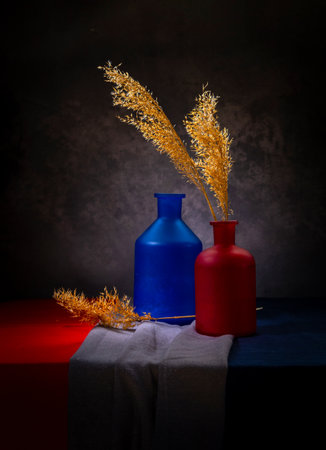 Bright still life with dry grass in a red bottle on a dark background.の写真素材