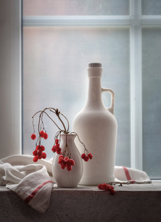 Still life with a white bottle and viburnum in a vase on the windowsill.の写真素材