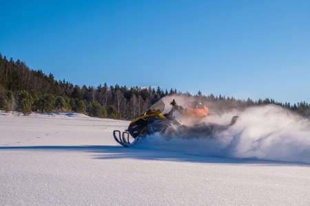 Athlete on a snowmobile moving in the winter forest in the mountains.