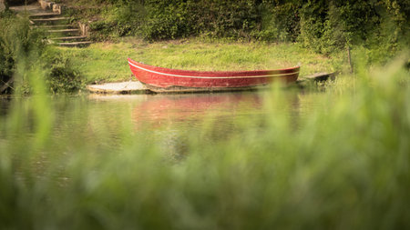 Red boat on the lake with green grass in the background. Selective focus.の写真素材