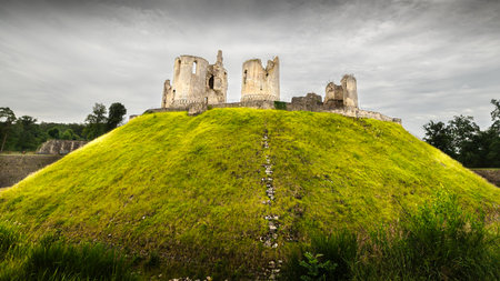 Ruins of medieval castle with green meadow and cloudy sky.の写真素材