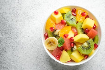 Bowl with homemade fresh fruit salad: mango, grapefruit, pomegranate, kiwi, banana on a light background top view copy space.の写真素材