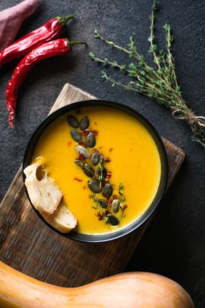 Homemade pumpkin cream soup with  seeds, spices and herbs on a dark background top view.の写真素材